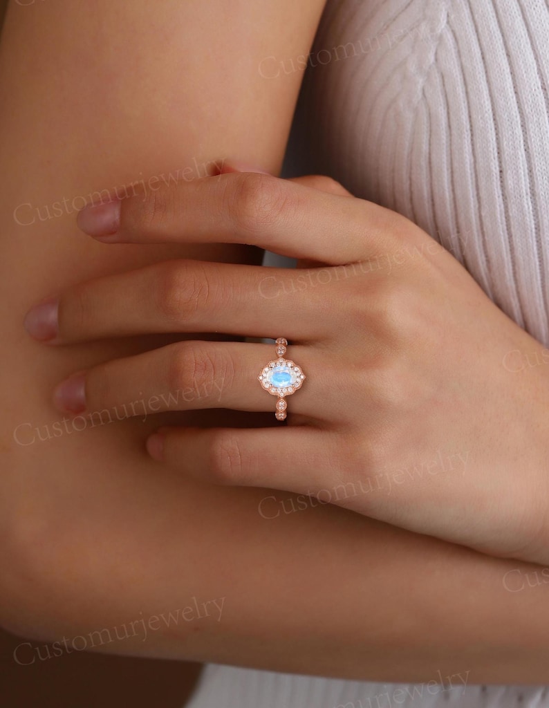 May include: Rose gold ring featuring a light blue oval gemstone, surrounded by a halo of smaller stones. The band has delicate detailing. A piece of jewelry.