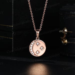 A delicate gold-toned necklace with a round pendant featuring a crescent moon design and three small stars.