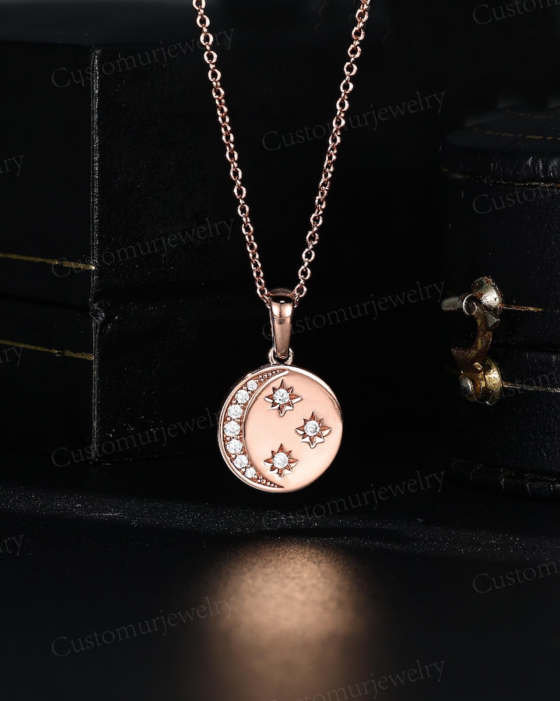 A delicate gold-toned necklace with a round pendant featuring a crescent moon design and three small stars.