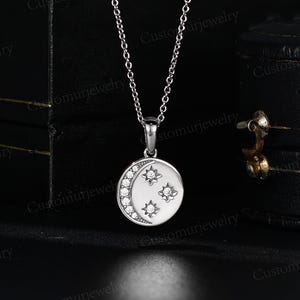 A silver necklace with a pendant featuring a crescent moon and three small stars.