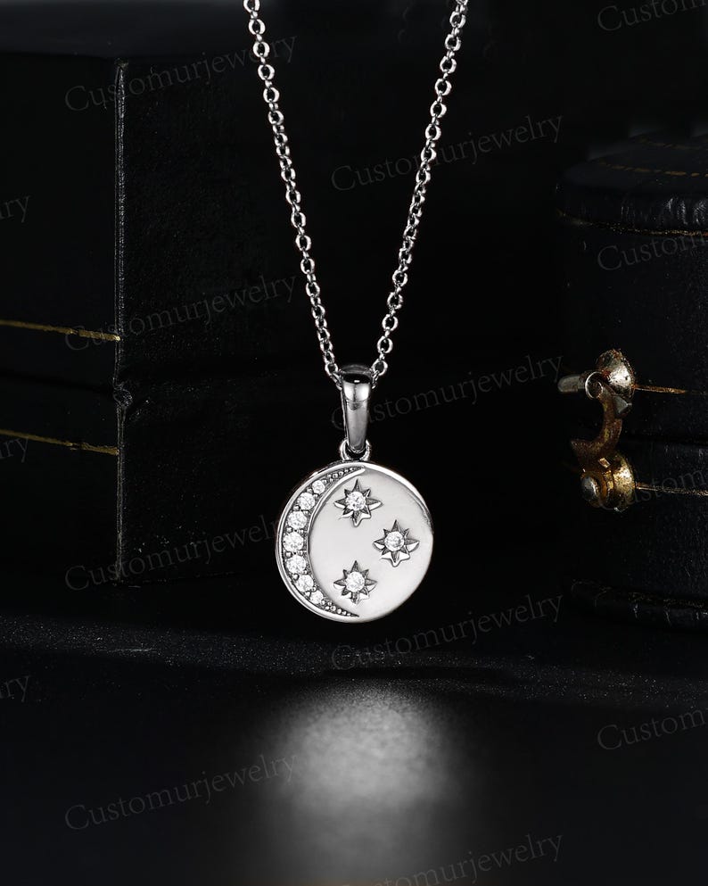 A silver necklace with a pendant featuring a crescent moon and three small stars.
