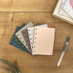 Könnte beinhalten: Ein Satz von sechs verschiedenen farbigen Papier-Nachfülleinsätzen für einen Disc-gebundenen Planer. Die Einsätze sind in den Farben Grün, Braun, Grau und Rosa gehalten. Die Einsätze haben Löcher an der linken Seite zum Binden.