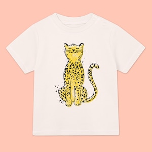 Może przedstawiać: Biała koszulka z krótkim rękawem z nadrukiem w postaci żółtego i czarnego lamparta.