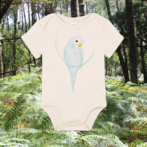 Może przedstawiać: Kremowy śpioszek dla niemowląt z ilustracją jasnoniebieskiego papużki na przodzie. Papużka siedzi na gałęzi i ma żółty dziób.