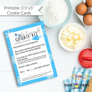 May include: A blue and white printable 3.5" x 5" cookie card with instructions for a "Do It Yourself Cookie Kit". The card features a blue snowflake design and the text "Keep cookie kit at room temperature. When ready to decorate gently massage icing bags to remove any natural separation. To use icing cut a VERY small hole at the tip of the icing bag. "Start small" you can always cut a larger hole later if desired. The larger the hole the faster the icing will flow from the bag. Decorate cookies as desired. Have fun and enjoy your cookies and tag us."