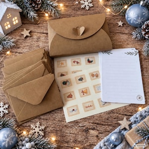 Könnte beinhalten: Ein Set aus braunen Kraftpapierumschlägen, ein gefalteter Umschlag mit herzförmigem Verschluss, ein Bogen mit kleinen quadratischen Aufklebern mit weihnachtlichen Motiven und ein Stapel weißes, liniertem Briefpapier mit grünen Blattakzenten.