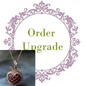 May include: A gold-toned pendant necklace featuring a heart-shaped pendant filled with red gemstones and surrounded by small white gemstones. The necklace is displayed with the words "Order Upgrade" in green text.