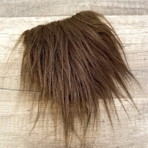 May include: A brown faux fur patch with long, soft fibers. The fur is thick and fluffy, and the patch is about 6 inches wide and 8 inches long.