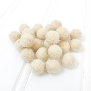 May include: A pile of off-white felt balls. The balls are soft and fluffy, and they are perfect for crafting or decorating.