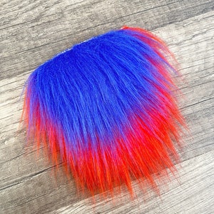 Op de afbeelding: Een blauwe en rode ombre-vachtstrook. De vacht is lang en pluche, met een gradi&euml;nt van blauw naar rood.