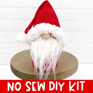 Puede incluir: Un kit de gnomo de bricolaje sin coser, rojo y blanco. El gnomo tiene un gorro rojo con un pomp&oacute;n blanco y una barba blanca. El gnomo est&aacute; sentado sobre una base de madera.