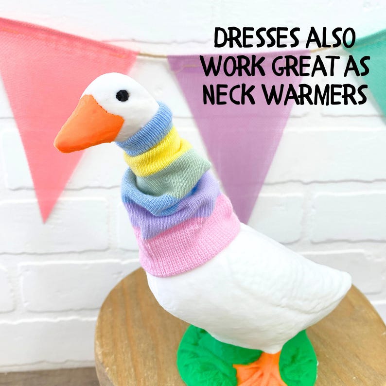 May include: A white goose figurine wearing a colorful striped neck warmer. The goose has an orange beak and feet, and is perched on a wooden surface. The text "Dresses also work great as neck warmers" is displayed above the goose.