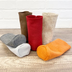 May include: Five felt fabric storage containers in different colors: gray, brown, red, beige, and orange. The containers are cylindrical and have a smooth, soft texture.