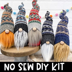 May include: Five handmade gnome decorations with long, curly beards and patterned knit hats. The gnomes have wooden noses and varying beard colors, including orange, gray, and blonde. The base is a wooden stand. The text "NO SEW DIY KIT" is at the bottom.