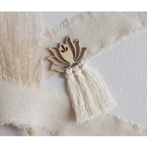 Könnte beinhalten: Ein Holz-Lotusblüten-Ausschnitt mit einem weißen Makramee-Quaste, der von unten hängt. Die Lotusblume ist ein Symbol für Reinheit, Erleuchtung und Wiedergeburt.