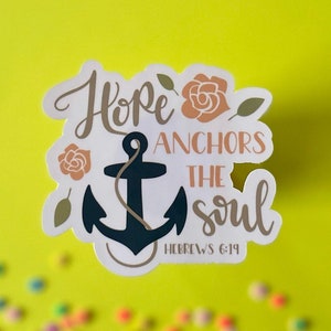 May include: A white sticker with a navy blue anchor, gold lettering, and pink flowers. The text reads "Hope anchors the soul, Hebrews 6:19".
