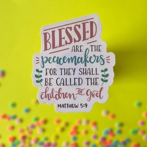 May include: A white sticker with a green, pink, and blue design. The sticker says "Blessed are the peacemakers for they shall be called the children of God" and "Matthew 5:9".