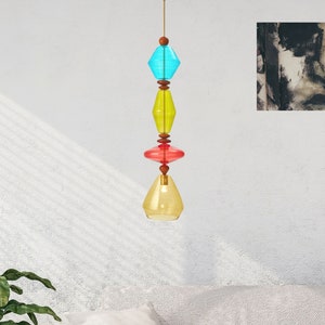 May include: A colorful glass pendant light fixture with a blue, yellow, and red geometric design. The light fixture is hanging from a white ceiling.