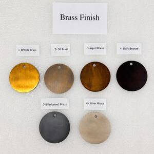 Peut inclure: Une collection de six disques m&eacute;talliques circulaires pr&eacute;sentant diverses finitions &eacute;tiquet&eacute;es Brass Finish. Les &eacute;tiquettes incluent 1- Bronze Brass, 2- Oil Brass, 3- Aged Brass, 4- Dark Bronze, 5- Blackened Brass et 6- Silver Brass, chacun avec un petit trou.