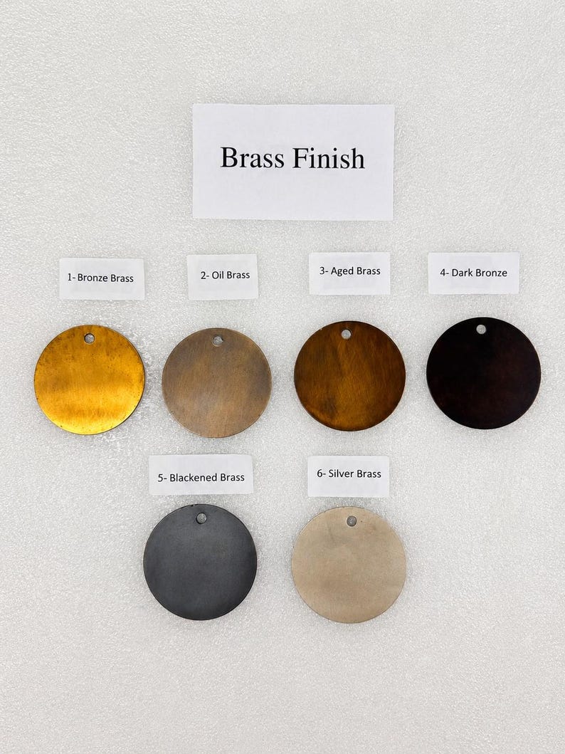 Peut inclure: Une collection de six disques m&eacute;talliques circulaires pr&eacute;sentant diverses finitions &eacute;tiquet&eacute;es Brass Finish. Les &eacute;tiquettes incluent 1- Bronze Brass, 2- Oil Brass, 3- Aged Brass, 4- Dark Bronze, 5- Blackened Brass et 6- Silver Brass, chacun avec un petit trou.