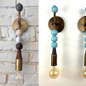 Peut inclure: Une applique murale compos&eacute;e d'une tige verticale en laiton orn&eacute;e de perles sph&eacute;riques empil&eacute;es aux couleurs et textures vari&eacute;es, incluant des tons bleus, beiges et bruns, termin&eacute;e par une douille cylindrique en laiton avec une ampoule claire.