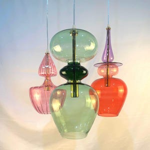 May include: Three glass pendant lights with different colored glass shades. The shades are green, pink, and red. The lights are hanging from a white ceiling.
