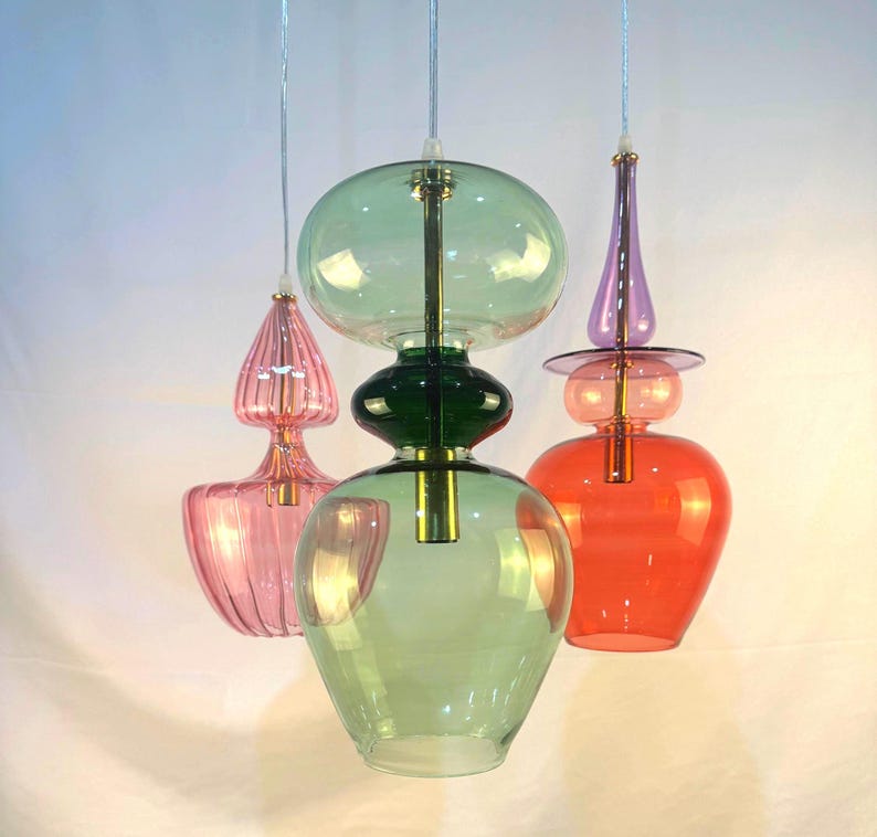 May include: Three glass pendant lights with different colored glass shades. The shades are green, pink, and red. The lights are hanging from a white ceiling.