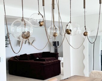 May include: A modern, multi-light chandelier with clear glass globes and brass accents hangs over a wooden dining table. The chandelier is suspended from the ceiling by multiple chains and cords.