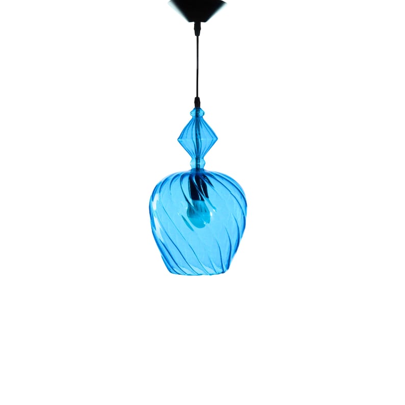 May include: A blue glass pendant light with a swirling design. The light is hanging from a black cord and has a clear light bulb inside.