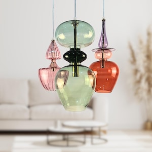 May include: A set of three glass pendant lights with different shapes and colors. The lights are hanging from the ceiling and are illuminated. The lights are in a living room setting.
