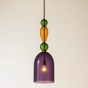 May include: A modern pendant light fixture with a purple bell-shaped shade and a decorative stem of green and yellow glass orbs. The light bulb is visible inside the shade, and the fixture hangs from a brown cord.