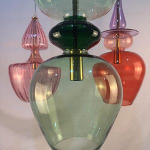 May include: Three glass pendant lights with a green, pink, and red color scheme. The lights are made of blown glass and have a unique, organic shape.