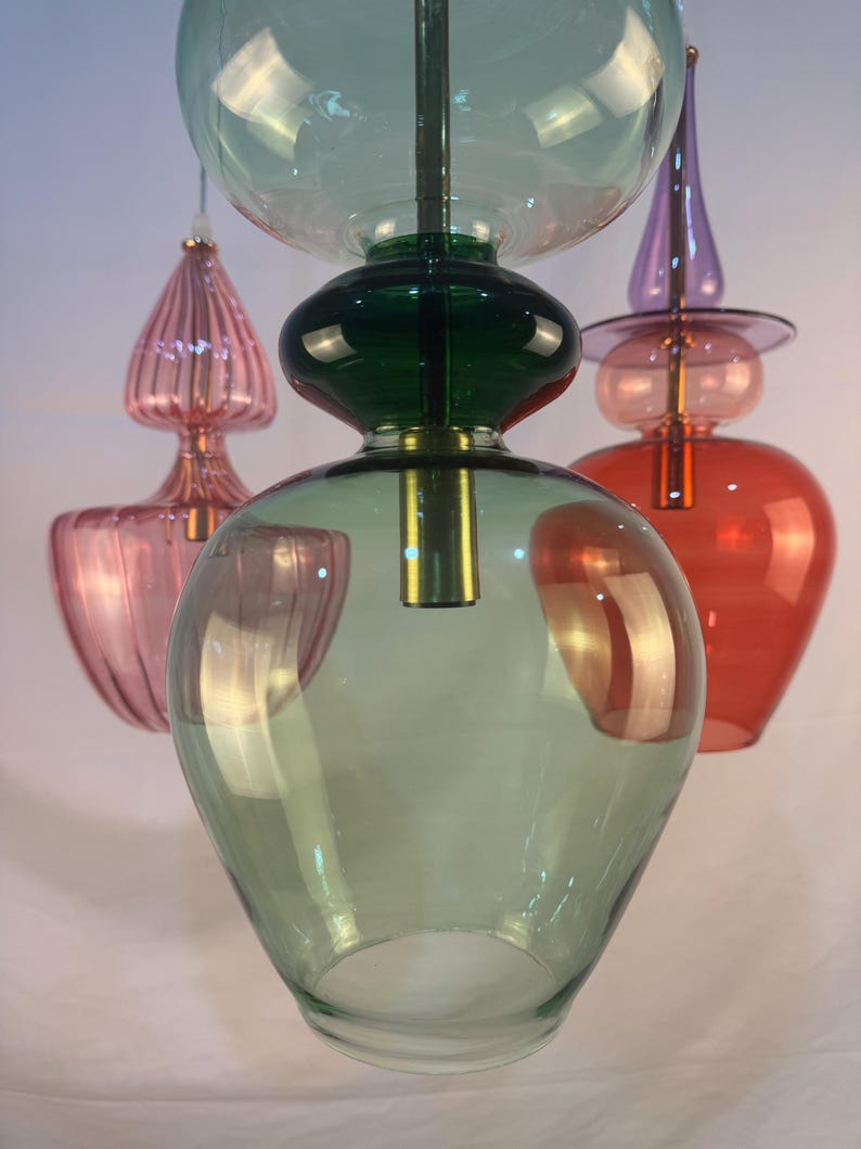 May include: Three glass pendant lights with a green, pink, and red color scheme. The lights are made of blown glass and have a unique, organic shape.