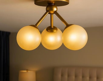 May include: A ceiling light fixture with three frosted glass globe shades. The fixture has a brass finish and is mounted on a ceiling. The light is on, illuminating the room with a warm glow. The fixture is a modern design.