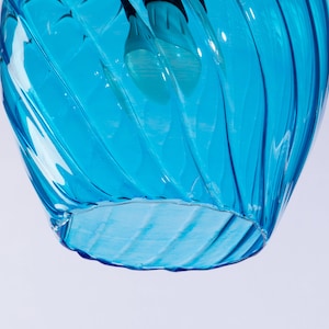 May include: A blue glass pendant light fixture with a swirling design. The light fixture is hanging from the ceiling and is illuminated by a light bulb.