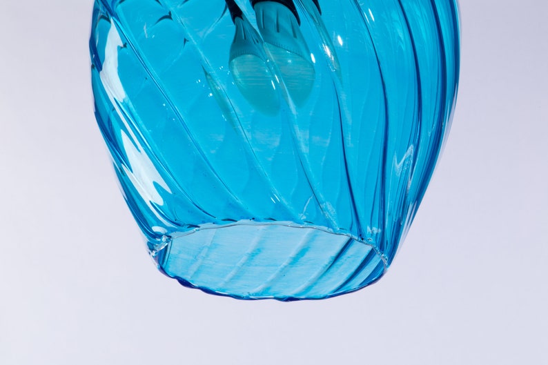 May include: A blue glass pendant light fixture with a swirling design. The light fixture is hanging from the ceiling and is illuminated by a light bulb.