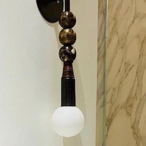 Peut inclure: Une applique murale compos&eacute;e d'une base circulaire noire, d'une tige verticale orn&eacute;e de trois sph&egrave;res empil&eacute;es en marbre brun fonc&eacute; et noir, d'une section m&eacute;tallique nervur&eacute;e et d'une ampoule ronde en verre d&eacute;poli blanc.