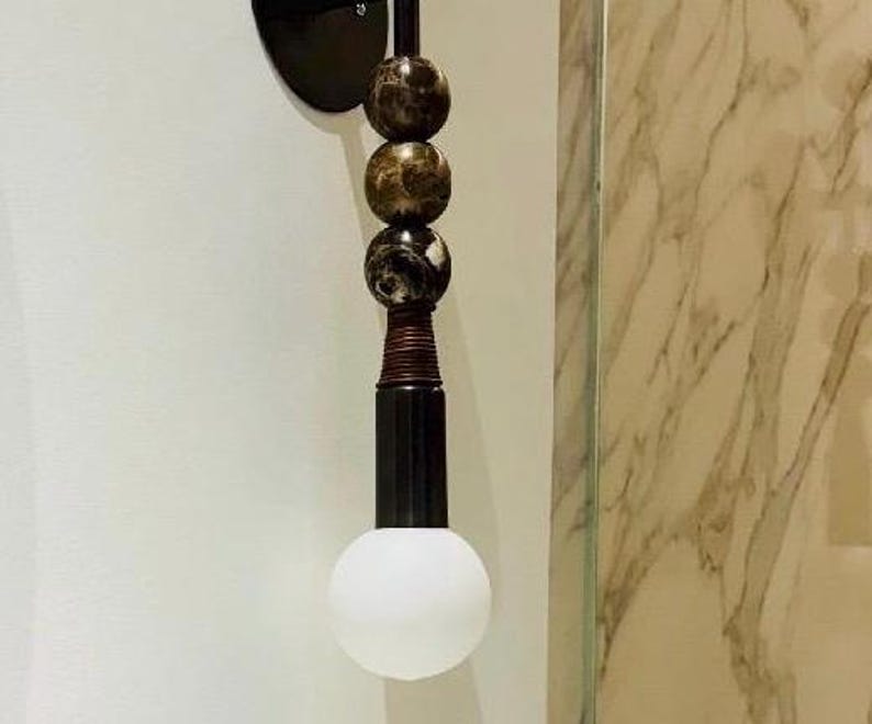 Peut inclure: Une applique murale compos&eacute;e d'une base circulaire noire, d'une tige verticale orn&eacute;e de trois sph&egrave;res empil&eacute;es en marbre brun fonc&eacute; et noir, d'une section m&eacute;tallique nervur&eacute;e et d'une ampoule ronde en verre d&eacute;poli blanc.
