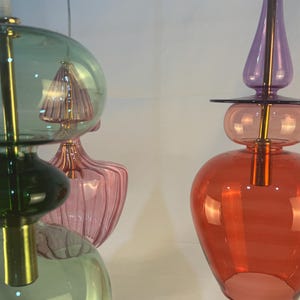 May include: Two multi-colored glass pendant lights with gold accents. The light on the left has green, pink, and clear glass shades. The light on the right has purple, pink, and red glass shades.