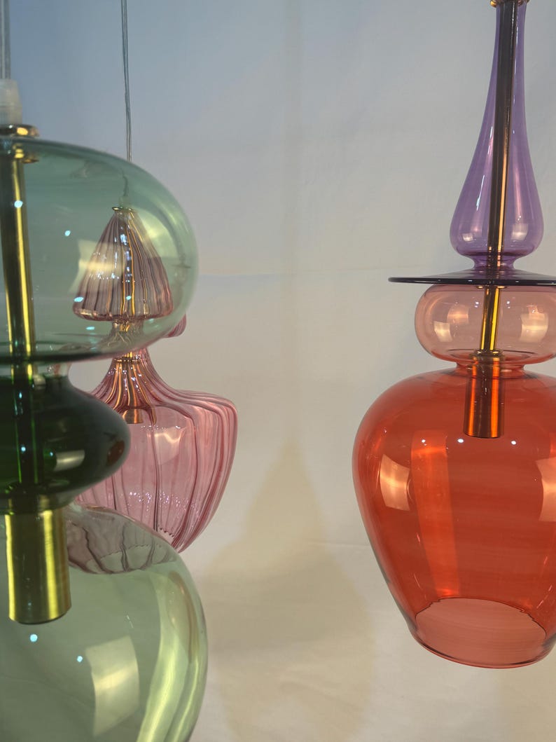 May include: Two multi-colored glass pendant lights with gold accents. The light on the left has green, pink, and clear glass shades. The light on the right has purple, pink, and red glass shades.