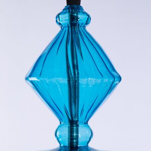 May include: A blue glass pendant light fixture with a diamond-shaped top and a round bottom. The light fixture has a black cord and a metal cap.