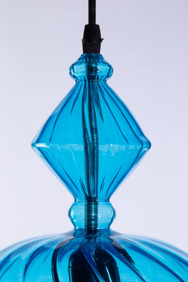 May include: A blue glass pendant light fixture with a diamond-shaped top and a round bottom. The light fixture has a black cord and a metal cap.