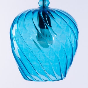 May include: A blue glass pendant light with a swirling design. The light is turned on and the bulb is visible.