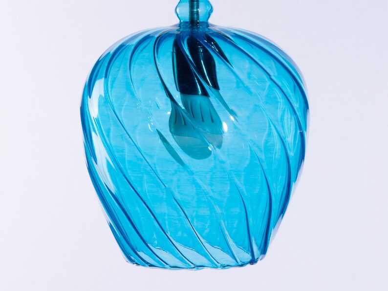 May include: A blue glass pendant light with a swirling design. The light is turned on and the bulb is visible.