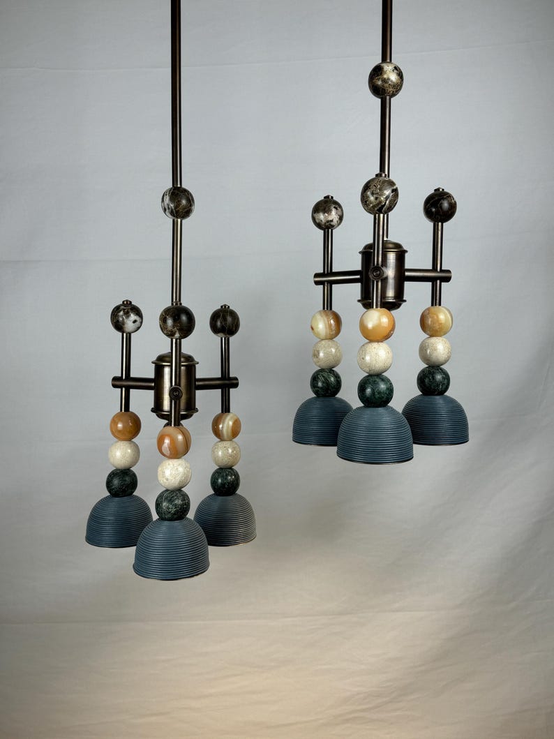 K&ouml;nnte beinhalten: Zwei moderne Pendelleuchten mit geometrischem Design. Jede Leuchte verf&uuml;gt &uuml;ber eine Reihe runder, bunter Perlen und drei blaue, glockenf&ouml;rmige Schirme.