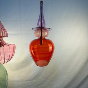 May include: A red, purple, and clear glass pendant light fixture with a unique, modern design. The light fixture has a round, bulbous shape with a pointed top and a small, round base.