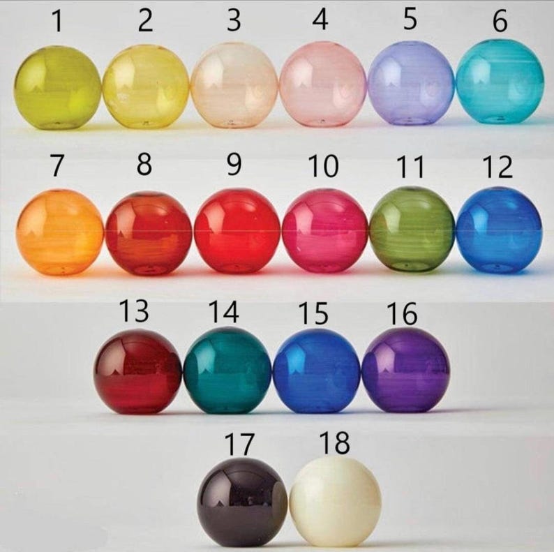 May include: A set of 18 colorful glass balls, numbered 1 through 18. The balls are arranged in three rows of six, with the numbers increasing from left to right. The balls are all different colors, including green, yellow, orange, red, pink, blue, purple, and white.