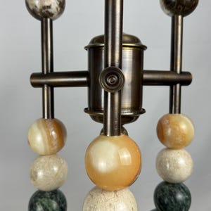K&ouml;nnte beinhalten: Ein Satz von drei Tischlampen im modernen Design. Jede Lampe besteht aus einem Stapel runder, bunter, marmorartiger Kugeln auf einem Messingfu&szlig;.