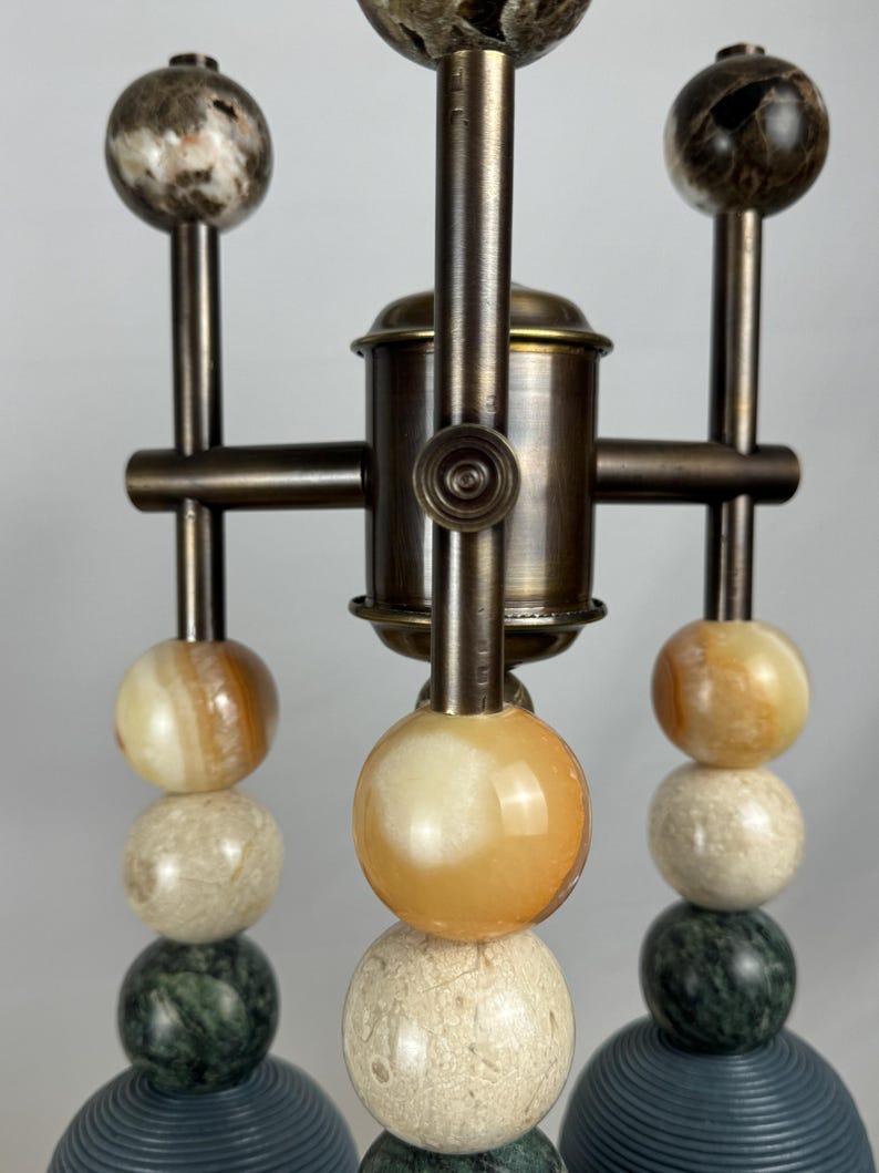 K&ouml;nnte beinhalten: Ein Satz von drei Tischlampen im modernen Design. Jede Lampe besteht aus einem Stapel runder, bunter, marmorartiger Kugeln auf einem Messingfu&szlig;.