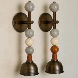 Peut inclure: Une paire d'appliques murales avec une plaque arri&egrave;re circulaire en bronze et une tige verticale orn&eacute;e de sph&egrave;res empil&eacute;es dans des tons gris, cr&egrave;me et ambre. La base de chaque luminaire est un abat-jour en bronze nervur&eacute; en forme de cloche.